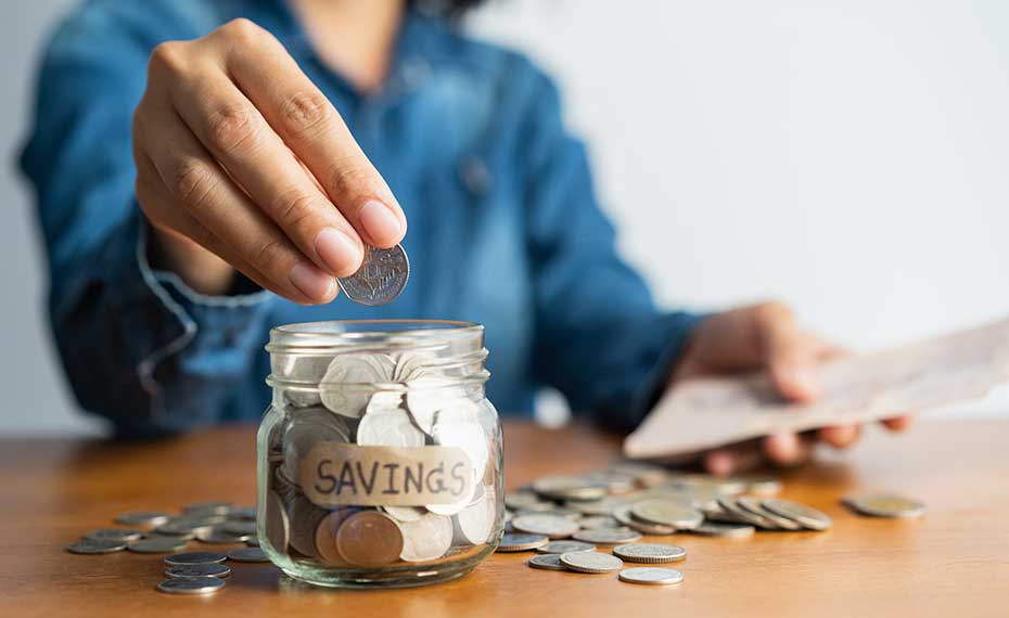 person putting coins in savings jar